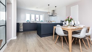 A modern kitchen with a central island, dark cabinetry, and a dining area with a wooden table and white chairs. - Modern town house situated in a quiet location with views across the harbour (Christchurch)