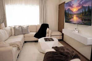 Un soggiorno moderno con un divano color beige, un tavolino da caffè bianco e una televisione a schermo piatto montata a parete.