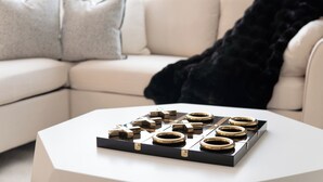 Un salon moderne avec un canapé blanc, un plateau décoratif noir et doré posé sur une table basse blanche, et un plaid en fausse fourrure noire.