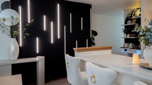 Une cuisine moderne avec un fond noir, des chaises blanches, un comptoir en bois et un panneau lumineux au néon.