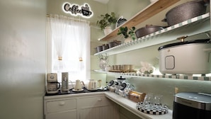 A kitchen with a coffee station, shelves with kitchenware, and a countertop with a coffee maker and toaster.