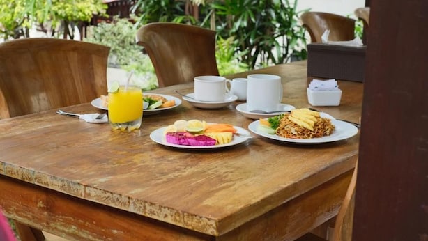 Una mesa de madera con platos de comida, un vaso de jugo de naranja y tazas blancas.