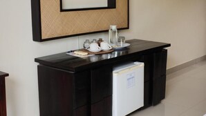 Un escritorio de madera oscura con un pequeño refrigerador, un cuadro enmarcado y varios objetos sobre la encimera.