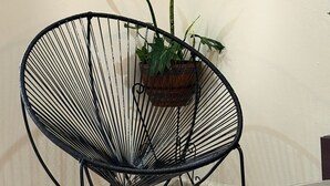 A black wireframe chair with a potted plant beside it, a wall clock, and a sign for 'Posada Azeneth Hotel Boutique Colonial'. - Posada Azeneth (Oxkutzcab)