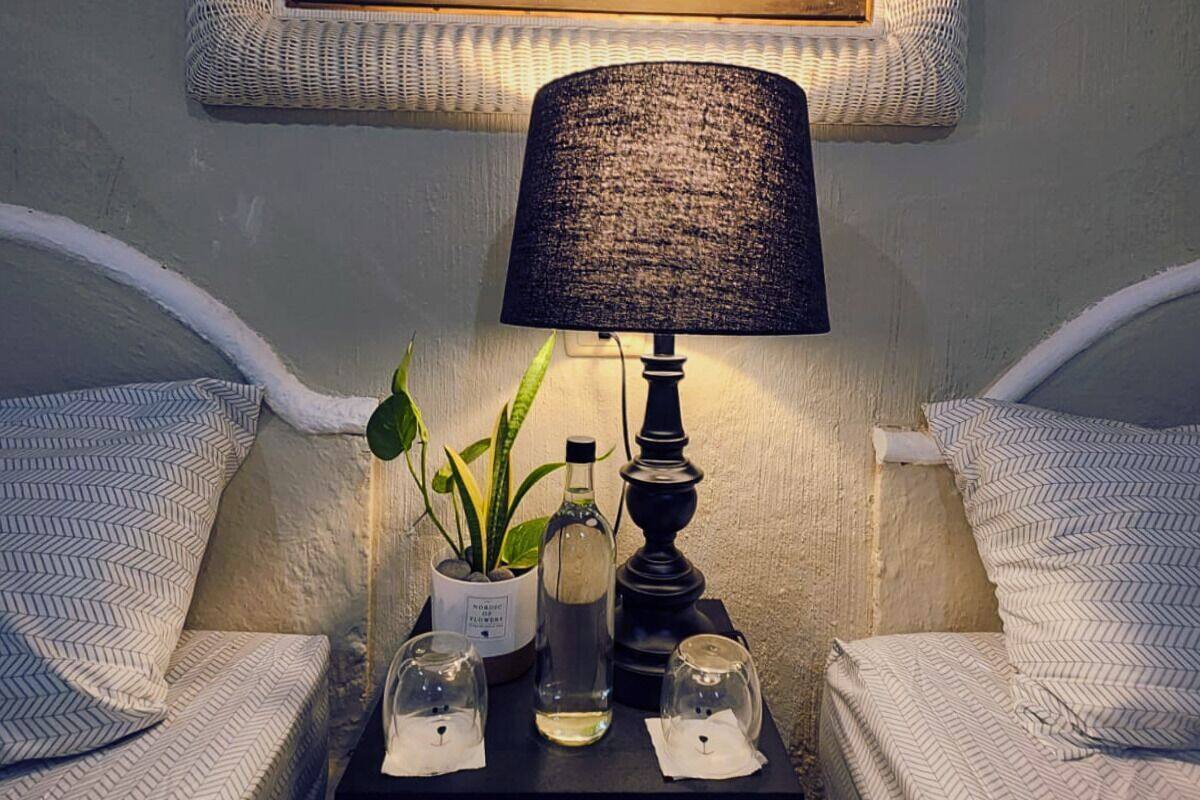 Ein Schlafzimmer mit zwei Betten, einem Nachttisch mit Lampe, einem gerahmten Gemälde und einer kleinen Topfpflanze.