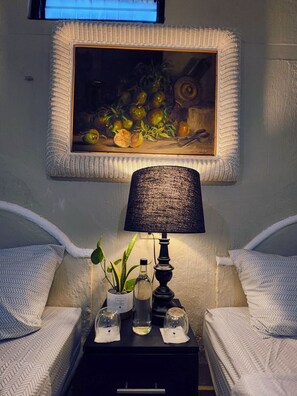 Une chambre avec deux lits, une table de chevet avec une lampe, un tableau encadré et une petite plante en pot.