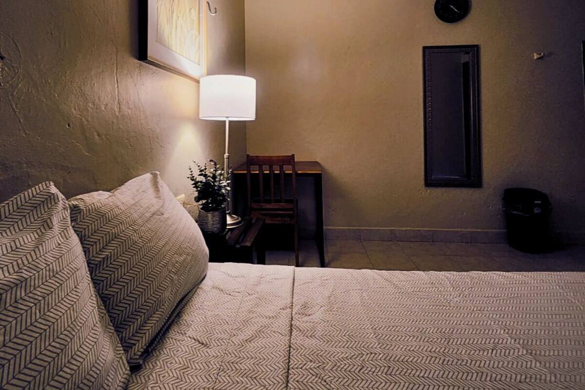 Ein Hotelzimmer mit Bett, Schreibtisch, Stuhl, Lampe, Klimaanlage und Wanduhr.