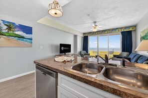 A kitchen with a dishwasher, double sink, and a ceiling fan. - Saltwater Luxe at Ocean Walk (Daytona Beach)