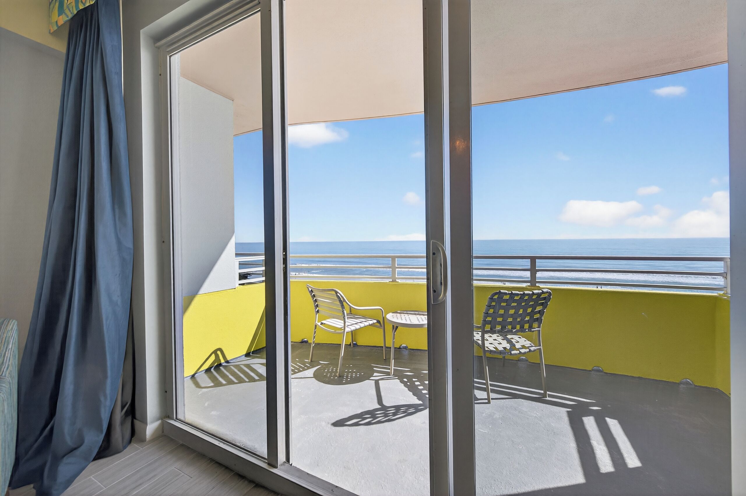 A balcony with a yellow wall, a glass door, and a view of the sea.