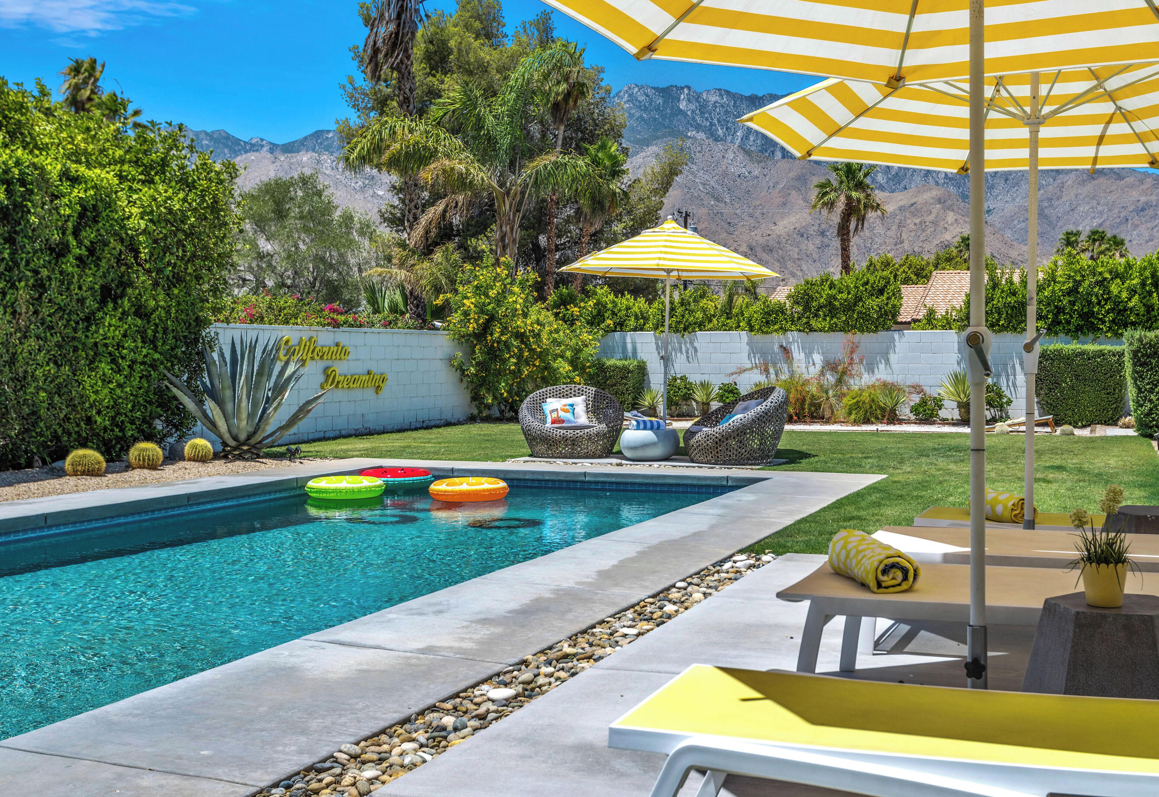 Une piscine avec des bouées gonflables, des chaises longues et un parasol jaune.
