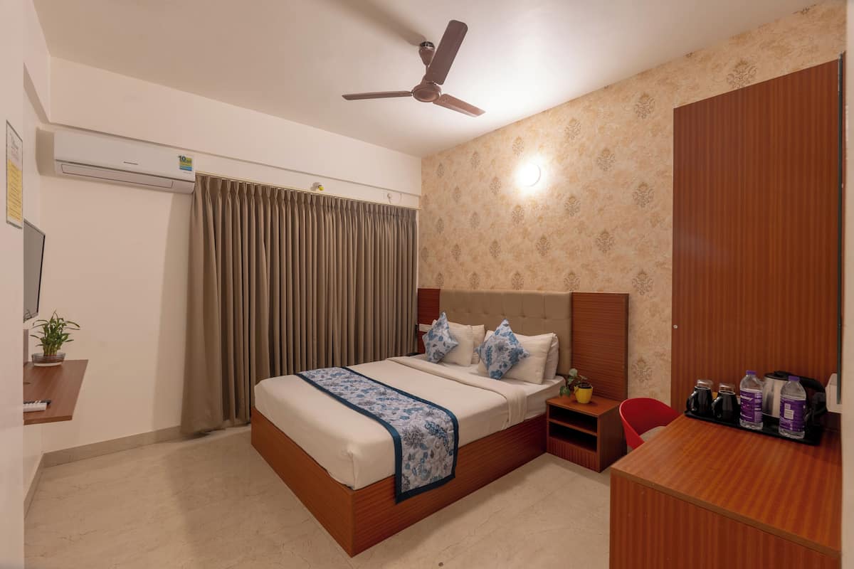 A hotel room with a bed, a desk, a chair, a wardrobe, a ceiling fan, and an air conditioning unit.