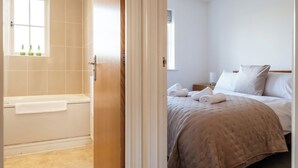A hotel room with a bathtub, a bed with a beige bedspread, and a window with a view. - Lovely 2 BD Home in Moreton-in-Marsh (Moreton-in-Marsh)
