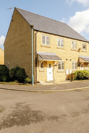A two-story stone building with a pitched roof, a visible chimney, and a small porch with a door. - Lovely 2 BD Home in Moreton-in-Marsh (Moreton-in-Marsh)