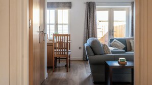 A living room with a sofa, a table, and a dining area with a chair and table. - Lovely 2 BD Home in Moreton-in-Marsh (Moreton-in-Marsh)