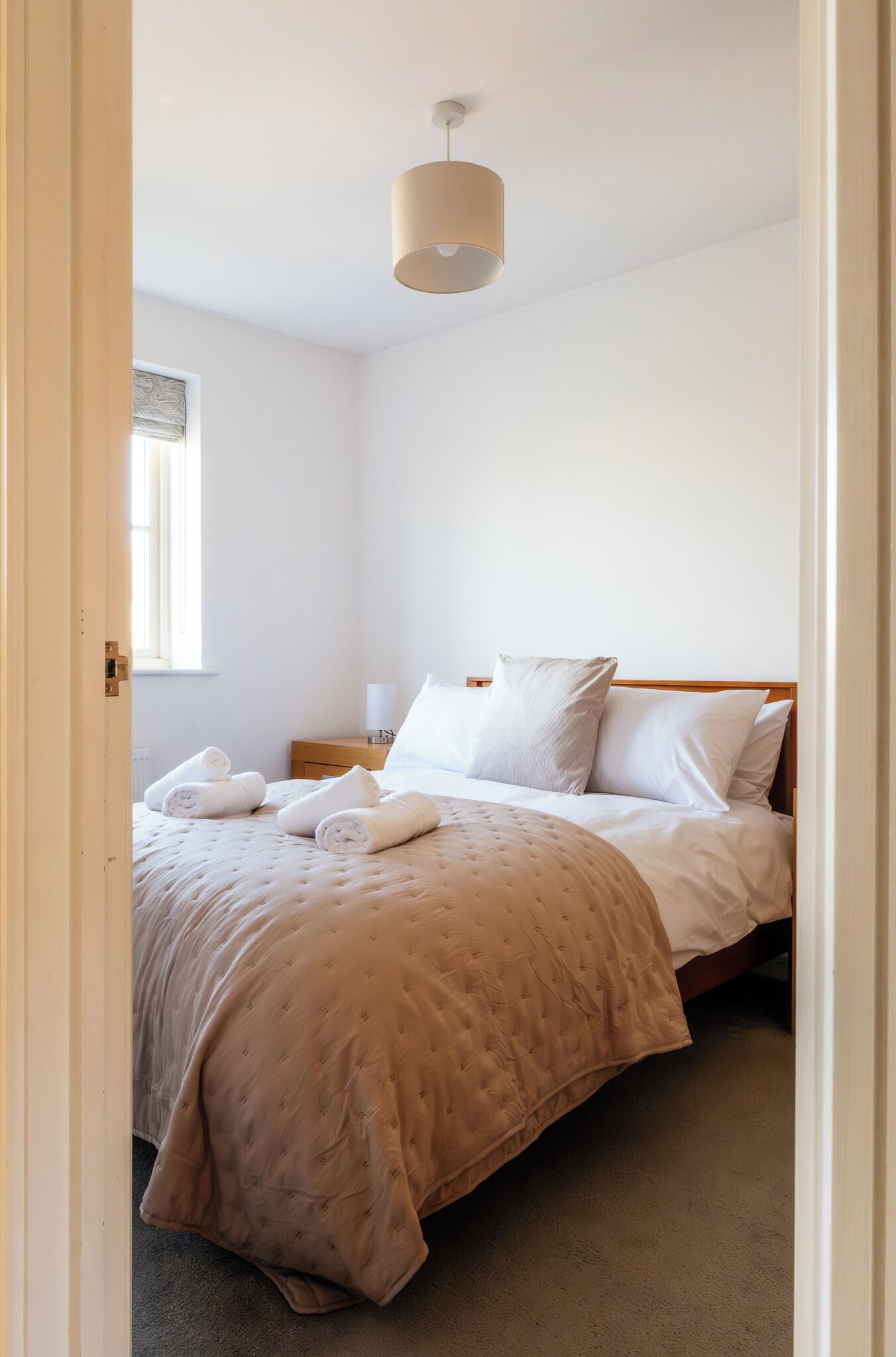 A bedroom with a bed, pillows, a bedside table, a lamp, and a window.