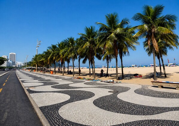 Eine Strandpromenade mit Palmen, einem Kachelweg und einer Stadtansicht im Hintergrund.