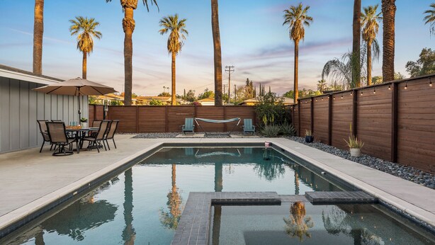 Une piscine avec une terrasse en bois, un hamac et de grands palmiers en arrière-plan.