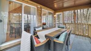 Una veranda coperta con mobili in vimini, un tavolo di legno e vista sugli alberi circostanti.