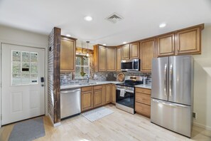 A modern kitchen with wooden cabinets, stainless steel appliances, and a window overlooking greenery. - Cozy Pocono Cabin w/ Hot Tub, Fire Pit & Game Room (Poconos lake)