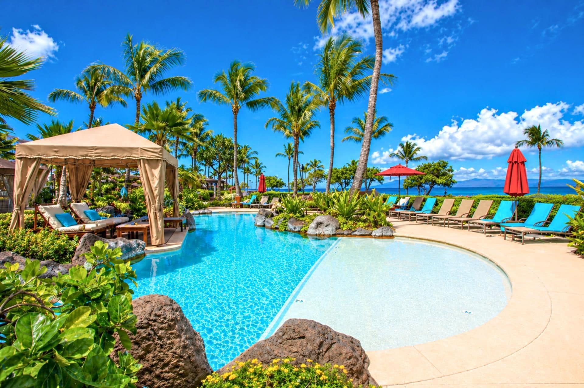 Ein Poolbereich mit Liegestühlen und Sonnensegel, umgeben von Palmen und blauem Himmel.