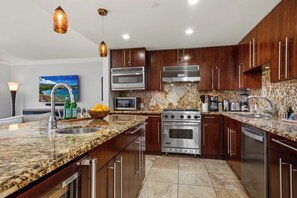 A modern kitchen with granite countertops, stainless steel appliances, and wooden cabinets. - Honua Kai | Ocean View 4 BR, Sleeps 12 | Car Incl. w/ 6+ Nights | HKH ML-2672 by KBM (Lahaina)