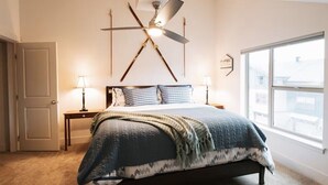 Ein Schlafzimmer mit einem Bett, zwei Nachttischen, einem Deckenventilator, einem Fenster und einer Tür.