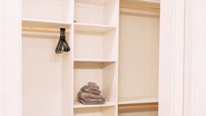 Ein begehbarer Kleiderschrank mit offenen Regalen, einer Kleiderstange und einem gefalteten Handtuch auf einem der Regale.