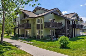 A multi-story residential building with a balcony on the second floor, a covered porch, and a well-maintained lawn. - Quail Run 3315 - Renovated, Hot Tub, Garage, W/D + EZCancel (Steamboat Springs)