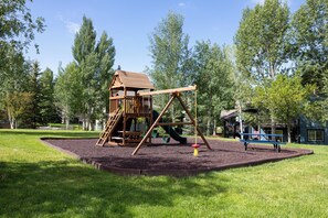 A playground with a wooden playhouse, swings, and a slide. - Quail Run 3315 - Renovated, Hot Tub, Garage, W/D + EZCancel (Steamboat Springs)