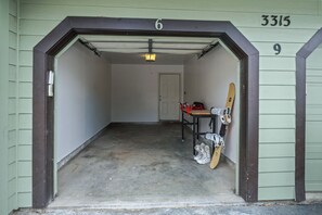 A garage with a door marked '6' and '9' above it, a concrete floor, and a table with a skateboard and a red bag. - Quail Run 3315 - Renovated Condo, Hot Tub, Garage, W/D (Steamboat Springs)