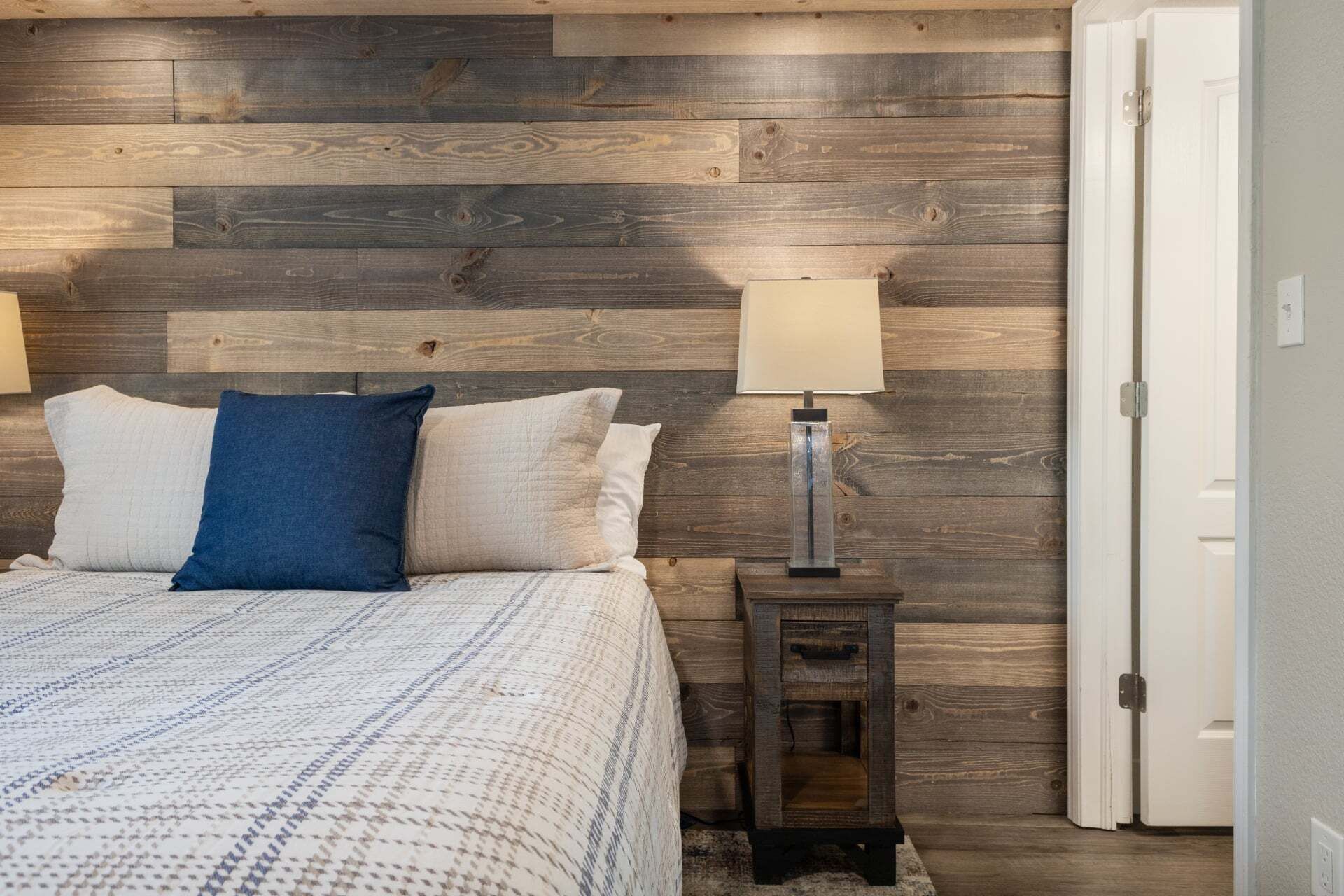 Une chambre à coucher avec une tête de lit en bois, un lit recouvert d’une literie à motifs, deux lampes de chevet et une table de chevet.