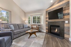 A living room with a fireplace, a sofa, a coffee table, and a television mounted on the wall. - Quail Run 3315 - Renovated, Hot Tub, Garage, W/D + EZCancel (Steamboat Springs)