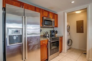 A kitchen with stainless steel appliances, wooden cabinets, a microwave, a kettle, and a washing machine. - 3 Honua Kai Villas | Ocean Front | Sleeps 16 | Free Car w/ 6+ Nights | ML-2720 (Lahaina)