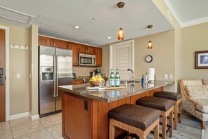 A kitchen with a central island, stainless steel appliances, and a seating area with a chair and ottoman. - Honua Kai | Ocean View 3 BR, Sleeps 10 | Car Incl. w/ 6+ Nights | HKH ML-2723 by KBM (Lahaina)