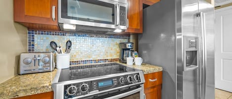 Uma cozinha com eletrodomésticos de aço inoxidável, armários de madeira, painel de azulejos e bancada de granito.