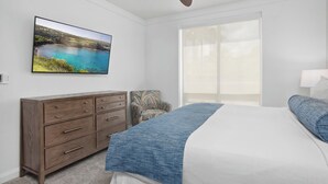 Un dormitorio con cama, cómoda, silla, ventilador de techo y un amplio ventanal.