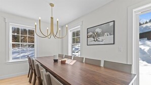 En matplats med ett träbord, stolar, en kristallkrona och stora fönster med utsikt över ett snötäckt landskap.