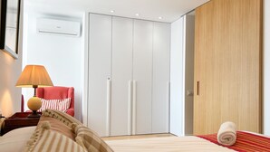 Een moderne hotelkamer met een bed, een rode stoel, een houten garderobe en een lamp.