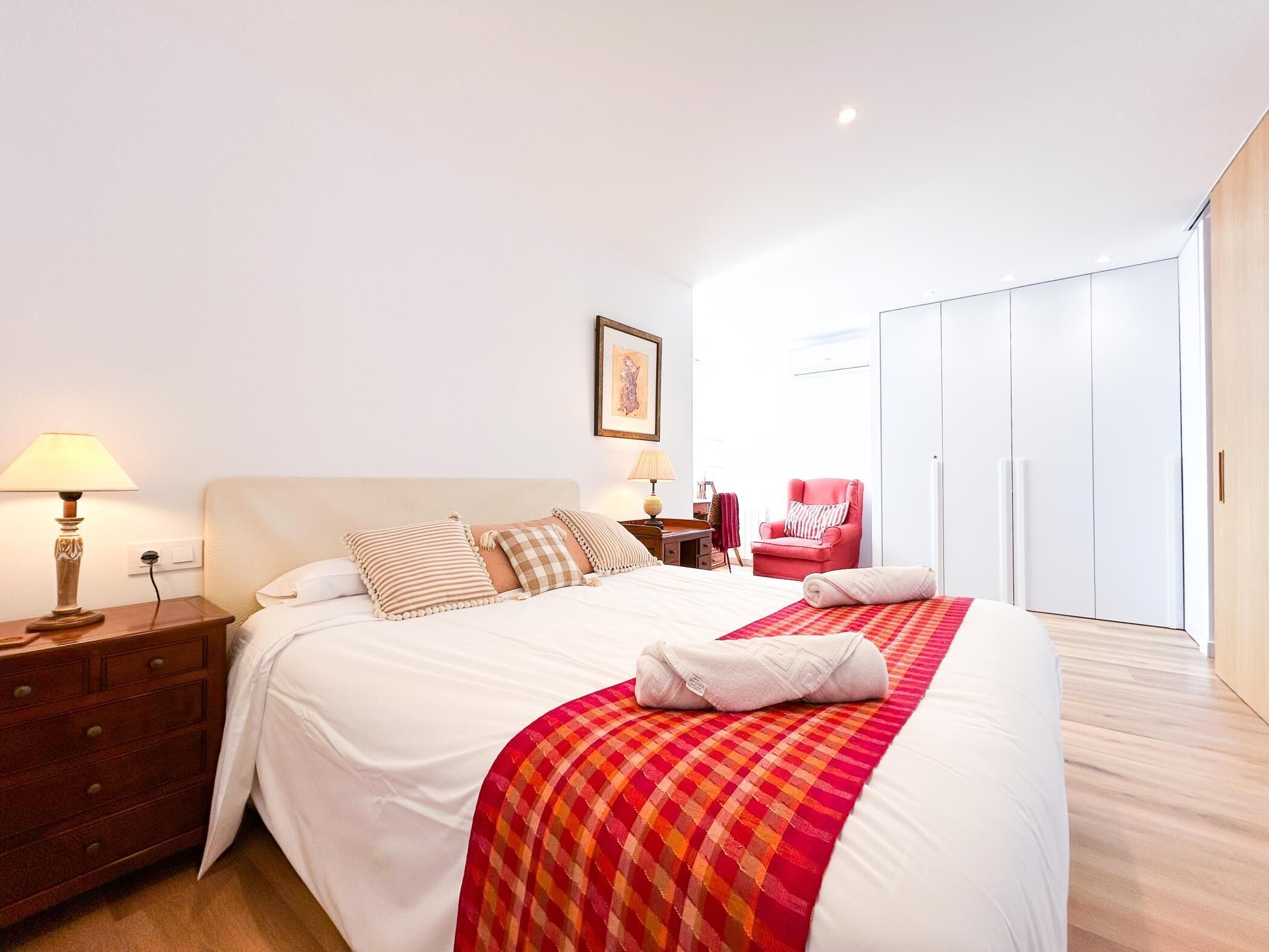 A hotel room with a bed, bedside tables, a chair, a wardrobe, and a painting on the wall.
