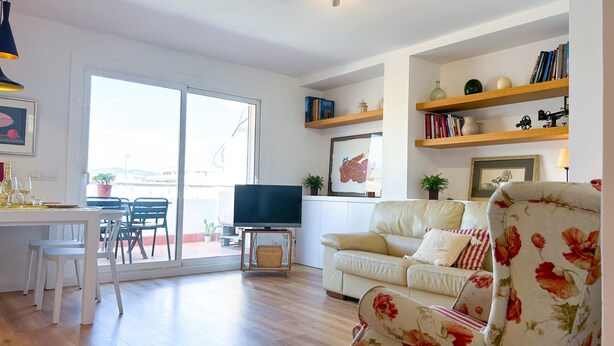 Een woonkamer met een bank, een televisie, een eettafel met stoelen en een balkon.