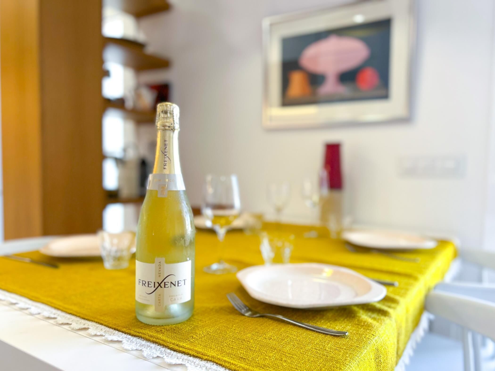 A dining table with a bottle of Freixenet cava, a white plate, and a fork.