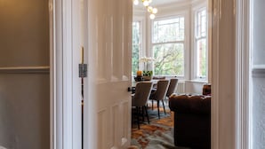 Un couloir mène à une salle à manger où se trouvent une table, des chaises et un canapé en cuir marron.