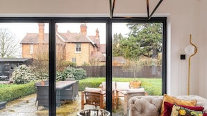 Un salon moderne doté d’une grande porte-fenêtre coulissante donnant sur un jardin arrière aménagé avec du mobilier d’extérieur et un espace vert.
