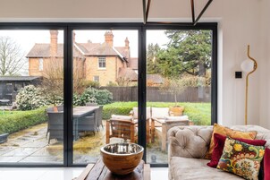 A modern living room with a large sliding glass door leading to a backyard with outdoor furniture and a garden.
