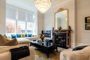 A living room with a sofa, a coffee table, a fireplace, a large mirror, and a chandelier.