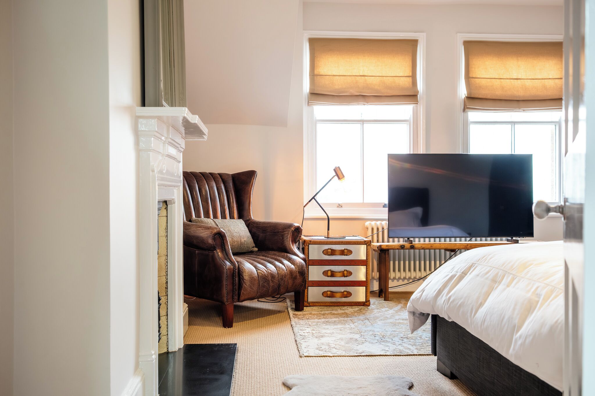 A bedroom with a leather armchair, a TV, a bedside table, and a radiator.