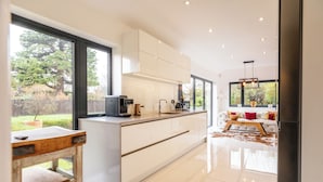 Une cuisine moderne dotée de grandes fenêtres, un coin repas avec un canapé et une table, et une vue sur l’extérieur.