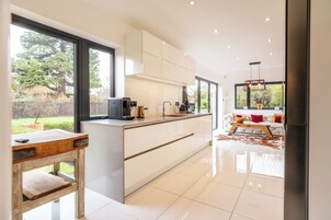 A modern kitchen with large windows, a dining area with a sofa and table, and a view of the outdoors.