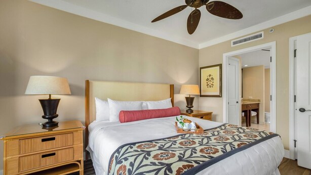 A hotel room with a bed, two bedside tables, a ceiling fan, a door, and a bathroom visible through an open door.
