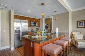 Una cocina moderna con una isla central, electrodomésticos de acero inoxidable, armarios de madera y una zona de estar con sillas de mimbre.